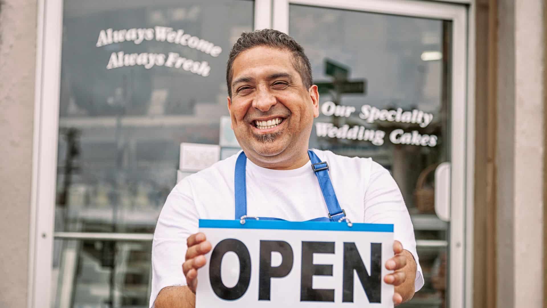 small business owner happily showing open sign outside his shop